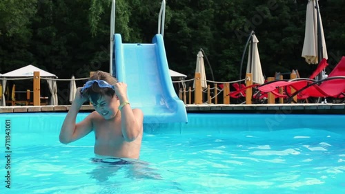 Little boy puts goggles standing waistdeep in water at swimming pool photo
