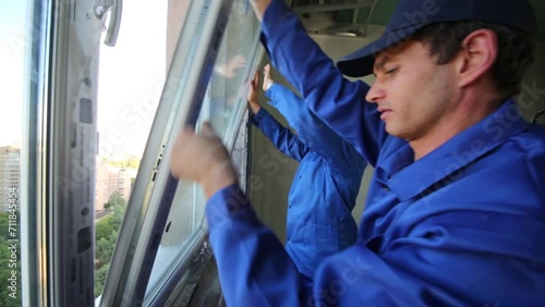 Two workers set window to new installed window-frame.
