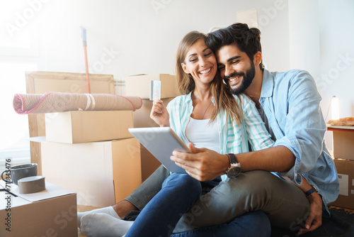 Smiling couple making online purchase using digital tablet in new apartment. Young couple, satisfied buyers holding credit card making convenient financial e-commerce payment digital transaction. photo