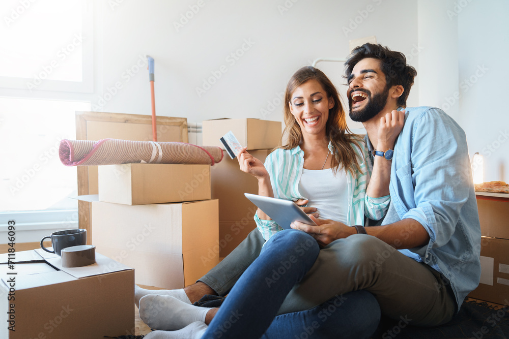 Enthusiastic millennial couple feeling excited using digital tablet, holding credit card, satisfied with online payment possibilities, rejoicing approved loan during relocation in new home. Enthusiastic millennial couple feeling excited using digital tablet, holding credit card, satisfied with online payment possibilities, rejoicing approved loan during relocation in new home.