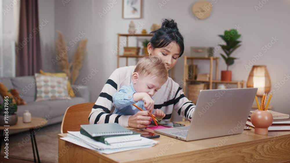 Woman freelancing while on maternity leave. Mother working at home with son on hands. LIttle boy drawing on paper. Mother taking care of kiddo and working with laptop. Young mom and child. Woman freelancing while on maternity leave. Mother working at home with son on hands. LIttle boy drawing on paper. Mother taking care of kiddo and working with laptop. Young mom and child.