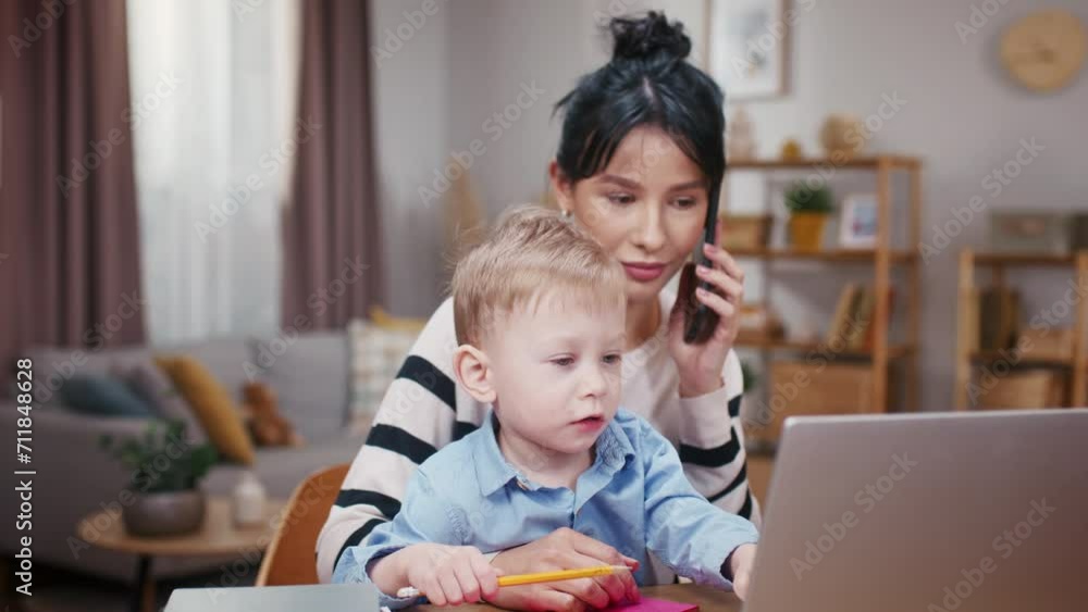 Mother taking care of little son and working at home. Little boy playing with table stuff. Woman resolving work issues while on maternity leave. Mother ending phone call and talking to son. Mother taking care of little son and working at home. Little boy playing with table stuff. Woman resolving work issues while on maternity leave. Mother ending phone call and talking to son.