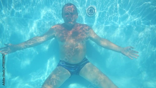 Elderly man sits on bottom of pure blue pool underwater photo