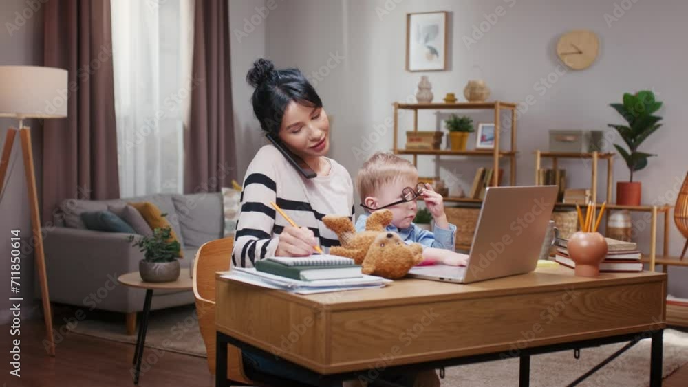 Mother taking care of little son and working at home. Woman talking by phone and holding kiddo. Woman resolving work issues while on maternity leave. Little boy playing with glasses on face. Mother taking care of little son and working at home. Woman talking by phone and holding kiddo. Woman resolving work issues while on maternity leave. Little boy playing with glasses on face.