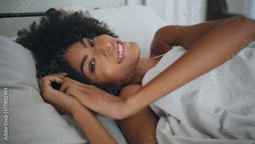 Portrait smiling model laying bed at home. Curly hair happy woman looking camera