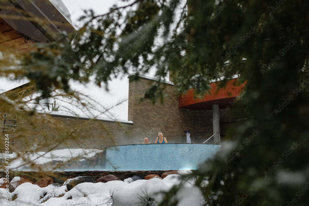An elderly woman and a man relax together in a swimming pool with hydromassage outdoors in winter. An elderly woman and a man relax together in a swimming pool with hydromassage outdoors in winter.