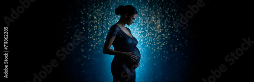 Banner with pregnant woman holding her hands on big belly ,A flickering magical light around the woman. Pregnancy, maternity, preparation,reproductology, expectation, copyspace for text, empty space  photo