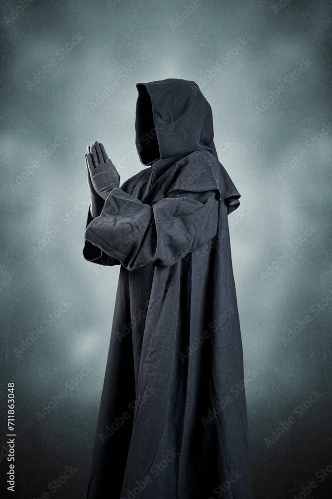 Medieval monk in hooded cloak praying in the dark