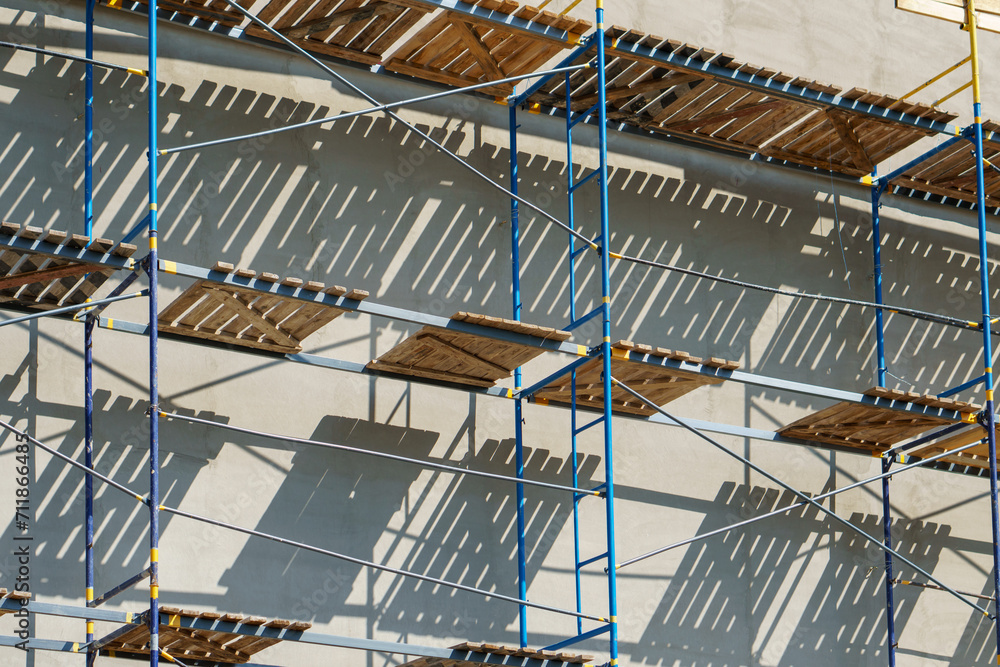 Naklejka premium Scaffolding is installed along the wall of the building under construction. Plastering and painting of the facade of the house. Metal supports and wooden platforms for working at height.
