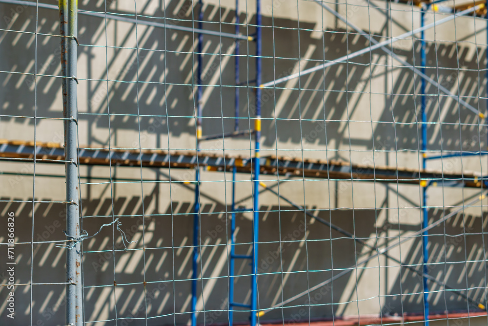 Scaffolding is installed along the wall of the building under construction. Plastering and painting of the facade of the house. Metal supports and wooden platforms for working at height.