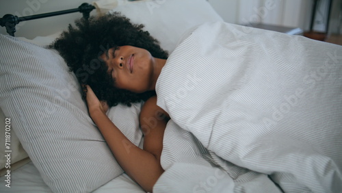 Drowsy model awaking at bed. Curly hairstyle sleepy woman hiding under blanket