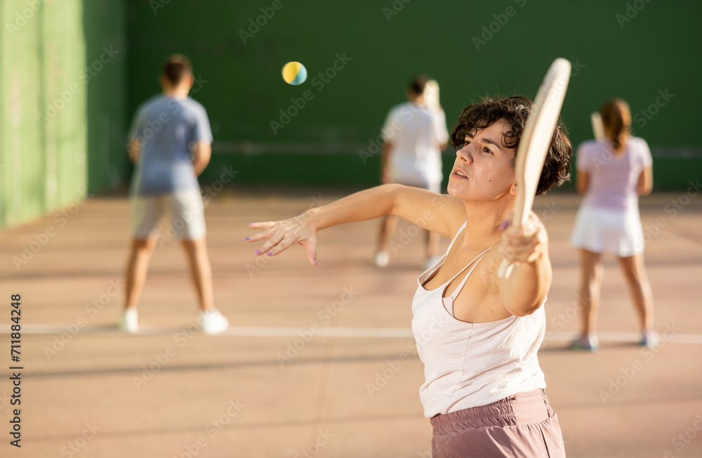 Latin woman serving ball with paleta during Basque pelota game outdoors. Woman playing pelota on outdoor fronton.