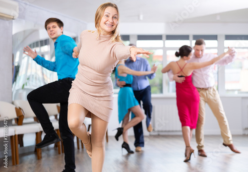 Group is of different ages active people engaged in Latin dance studio and learns movements of cha-cha-cha dance