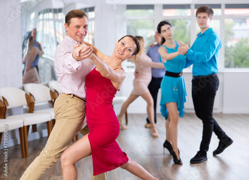 Positive people of different ages dancing tango in pairs in dance hall