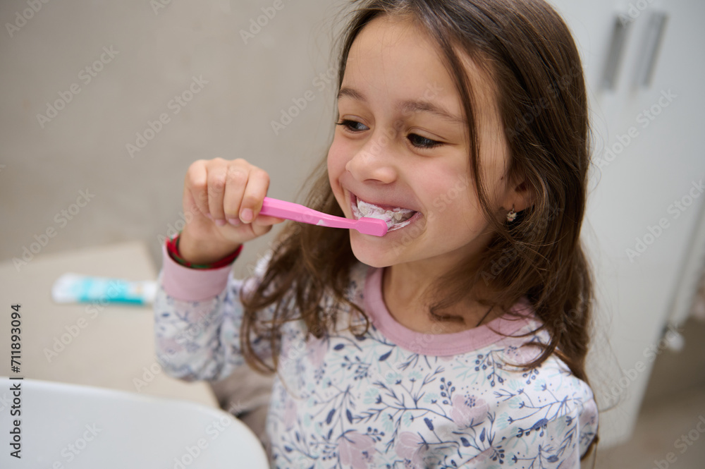 Adorable little child girl brushing teeth in front of the mirror in the home bathroom Adorable little child girl brushing teeth in front of the mirror in the home bathroom