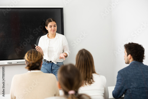 Young female professor explaining subject to classroom full of students