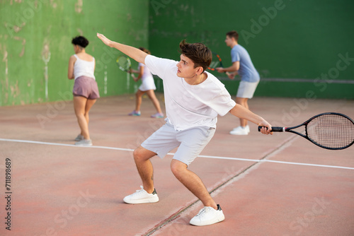 Caucasian young man serving ball during frontenis game outdoors. Boy playing pelota on outdoor fronton. © JackF