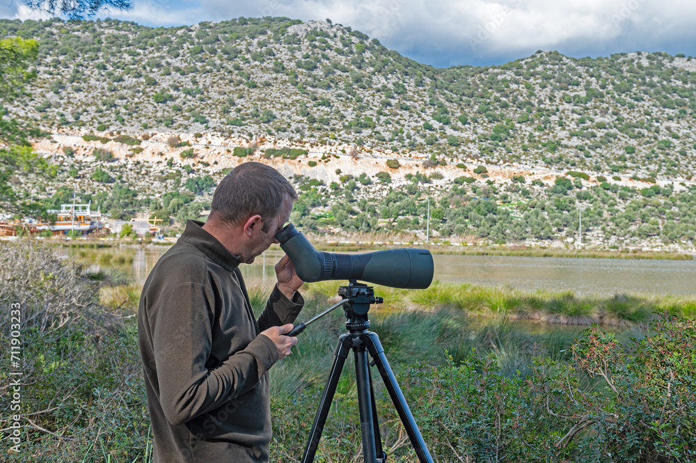 A man birdwatching in a lake with a telescope.