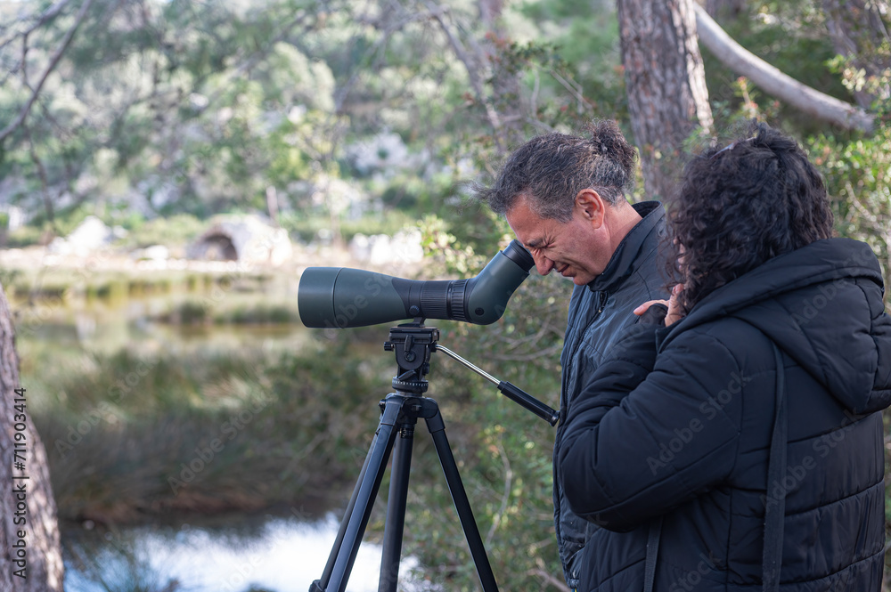 A man and a woman bird watching in the lake with a telescope.