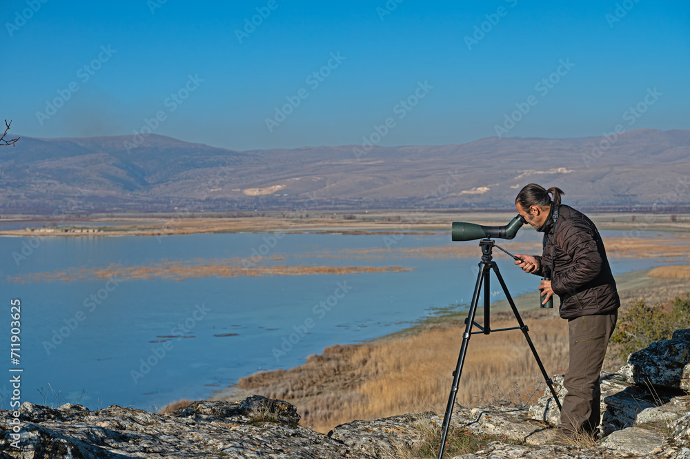 A man birdwatching in a lake with a telescope.