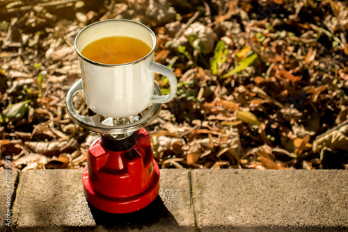 Obraz na płótnie A small tourist stove, for a gas cartridge. Cooking tea on a camping stove on the grass in autumn, in a parking lot, in a park. Chamomile tea outdoors. w salonie