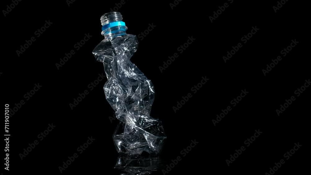 Pressed bottle trash on black background. A view of pressed plastic bottle spinning on the table against black background. A concept of trash plastic pollution in the Earth. Pressed bottle trash on black background. A view of pressed plastic bottle spinning on the table against black background. A concept of trash plastic pollution in the Earth.