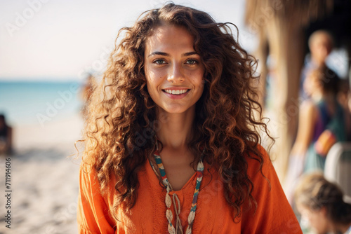 Generative AI image of a relaxed cheerful young woman with curly hair smiling looking at camera, dressed in a vibrant orange top enjoying a beautiful sunny day at the beach photo