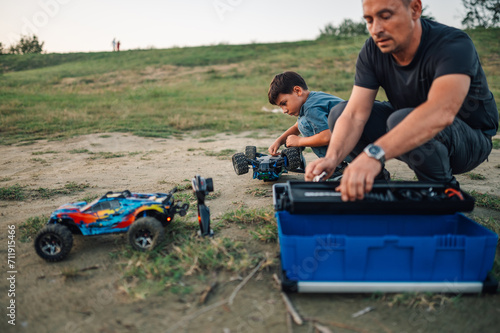 Father and son with fixing toy cars in nature.
