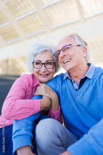 Vertical photo of a happy elder couple sitting and embracing in an urban space