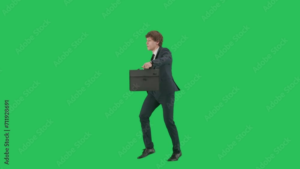 Portrait of male model in suit on chroma key green screen background. Side view, businessman in trendy suit walking and dancing with paper case. Portrait of male model in suit on chroma key green screen background. Side view, businessman in trendy suit walking and dancing with paper case.