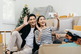 Young couple sitting on the sofa using smartphone to take a selfie at new home around cardboard boxes.