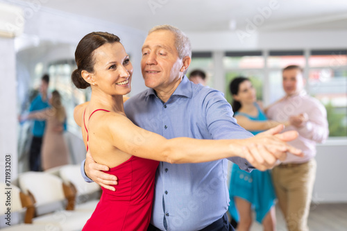 Positive people of different ages dancing tango in pairs in dance hall