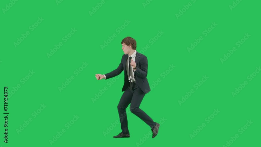 Profile view of male model in suit isolated on chroma key green screen background. Positive young businessman in blue suit walking making funny moves Profile view of male model in suit isolated on chroma key green screen background. Positive young businessman in blue suit walking making funny moves