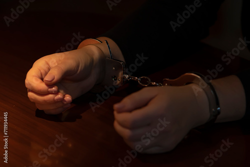 Hands of a woman in police handcuffs, dark tonality.