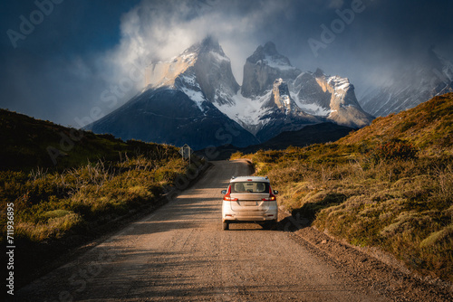 a car on a road to the snow mountain under clouds and sun light