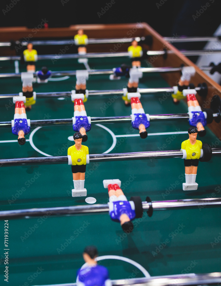 Fototapeta premium Group of friends playing kicker in a sports bar room, colleagues teammates play table football, table soccer game in the office, having fun, tabletop football match competition at work