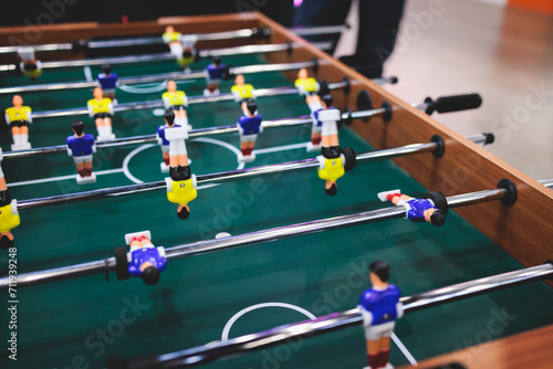 Group of friends playing kicker in a sports bar room, colleagues teammates play table football, table soccer game in the office, having fun, tabletop football match competition at work