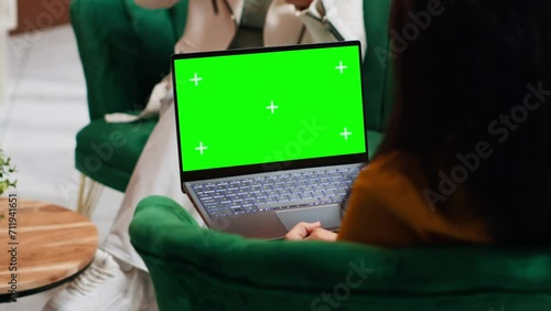 Hotel guest using laptop with greenscreen layout in lobby, looking at copyspace chromakey display in lounge area. Modern person holding pc showing isolated mockup template on screen. photo