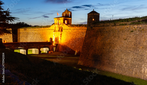 View of illuminated main gate with drawbridge and stone walls with corner bastions of medieval fortified pentagonal Ciudadela de Jaca, military fortress in Spanish province of Huesca in summer dusk photo