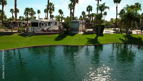 Aerial: Drone Shot Of Caravans Parked In Mobile Home Park, Drone Flying Backwards Over Fountain In Pond During Sunny Day - Palm Springs, California