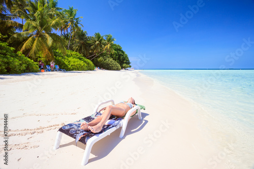Woman relaxing on a lounge chair on a tropical beach in the Maldives photo