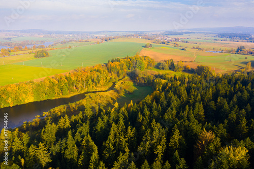 Aerial view of green, yellow and orange trees, fields and river in autumn
