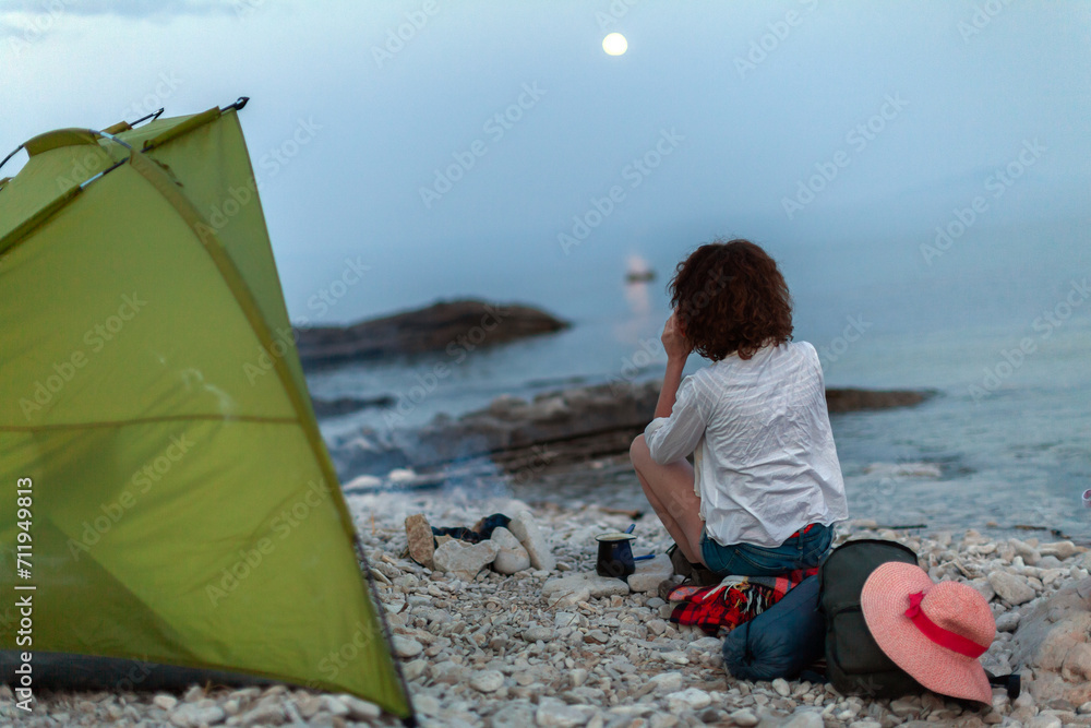 Woman Camping on a Beach Enjoying Moon Rising over Sea in Tranquility Woman Camping on a Beach Enjoying Moon Rising over Sea in Tranquility
