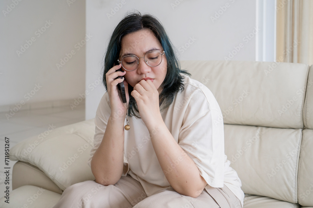 Sad overweight woman taking on a cellphone while sitting on sofa at home Sad overweight woman taking on a cellphone while sitting on sofa at home