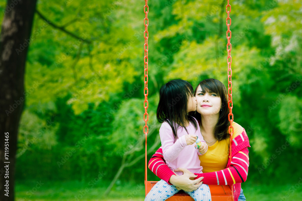 Daughter kissing mother while playing together in the playground Daughter kissing mother while playing together in the playground