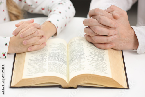 Girl and her godparent praying over Bible together at table indoors, closeup