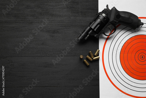 Shooting target, handgun and bullets on black wooden table, top view. Space for text