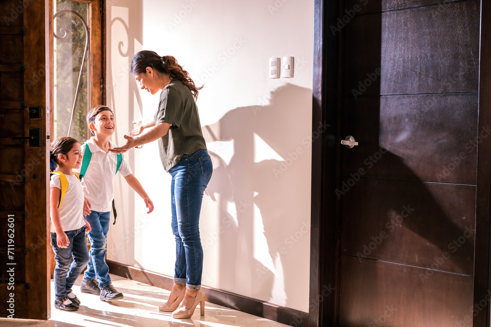 Two Latino children arrive from school and their mother receives them with love at the door of her home.