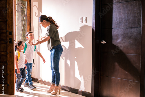Two Latino children arrive from school and their mother receives them with love at the door of her home.