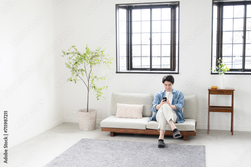 Fototapeta premium Wide angle of middle man on phone in living room Spring and summer image of a bright living room